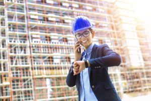 a woman with a construction hat talking on the phone and checking the time on her watch